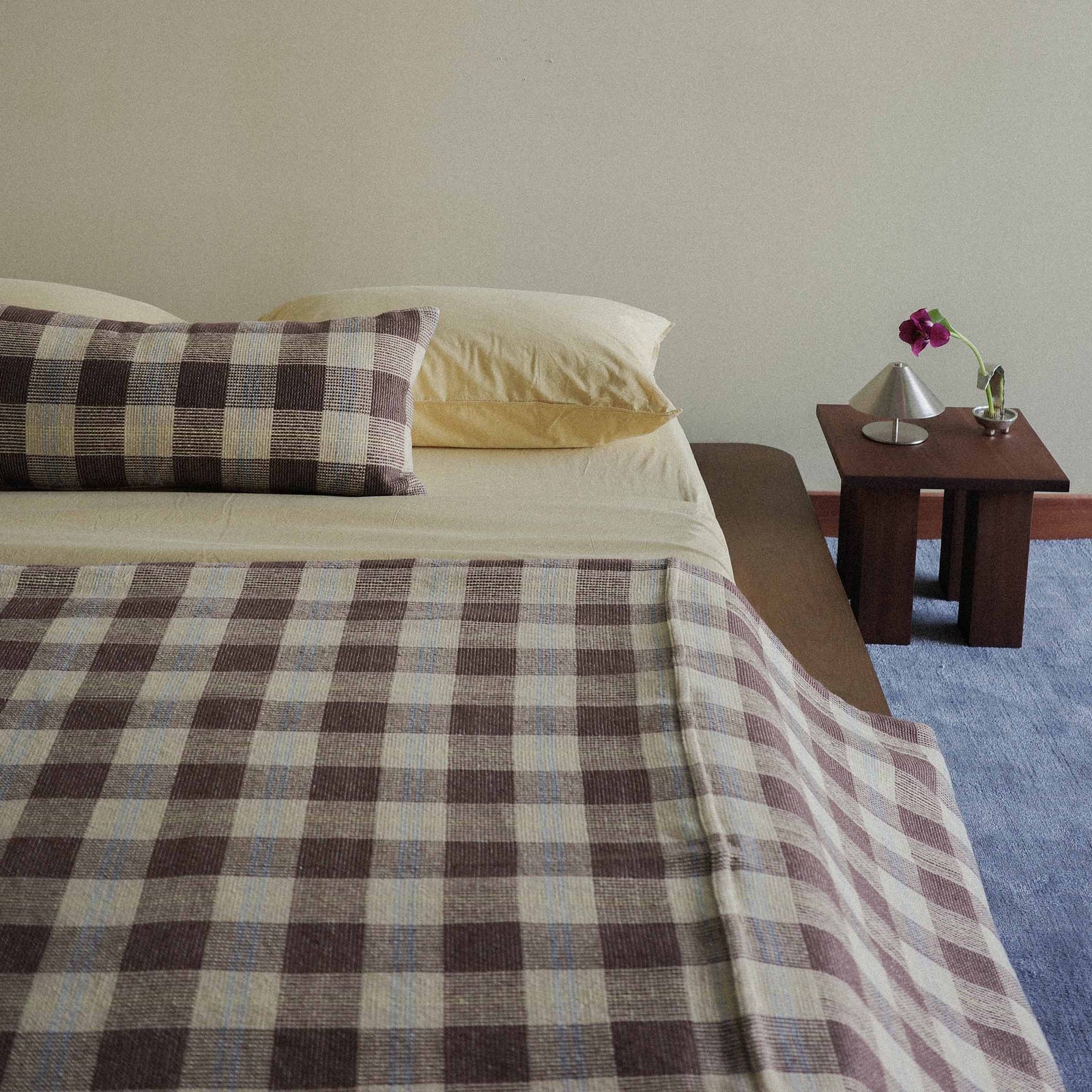 A neatly made bed with a checkred bedcover and yellow sheets
