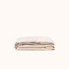 Folded beige Oat / cream fitted sheet made of matte sateen fabric, displayed against a white background