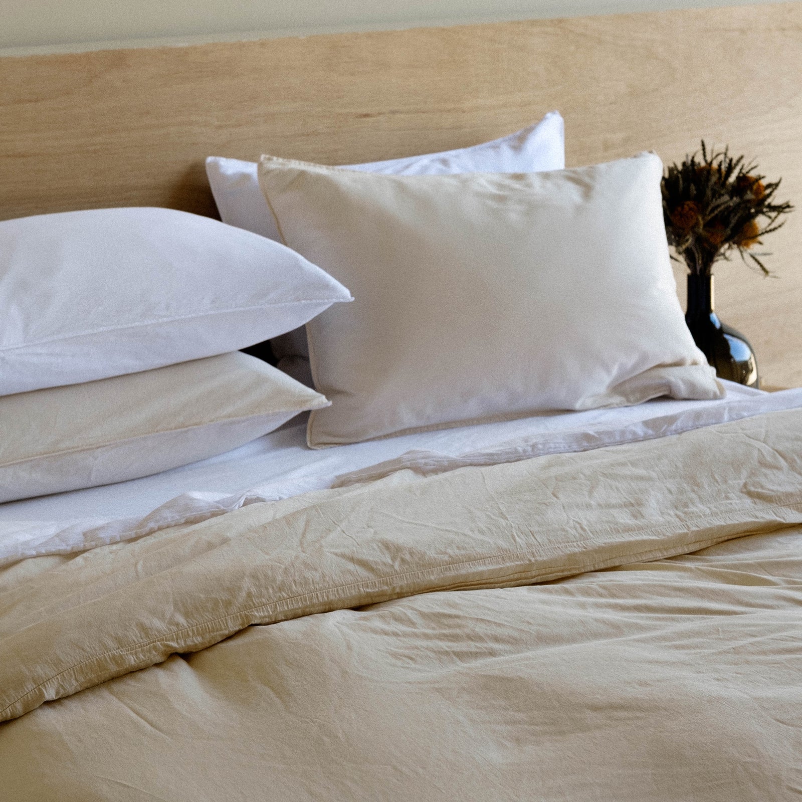 Close up of the top of a bed with beige and white matte sateen sheets and pillows in a bedroom setting